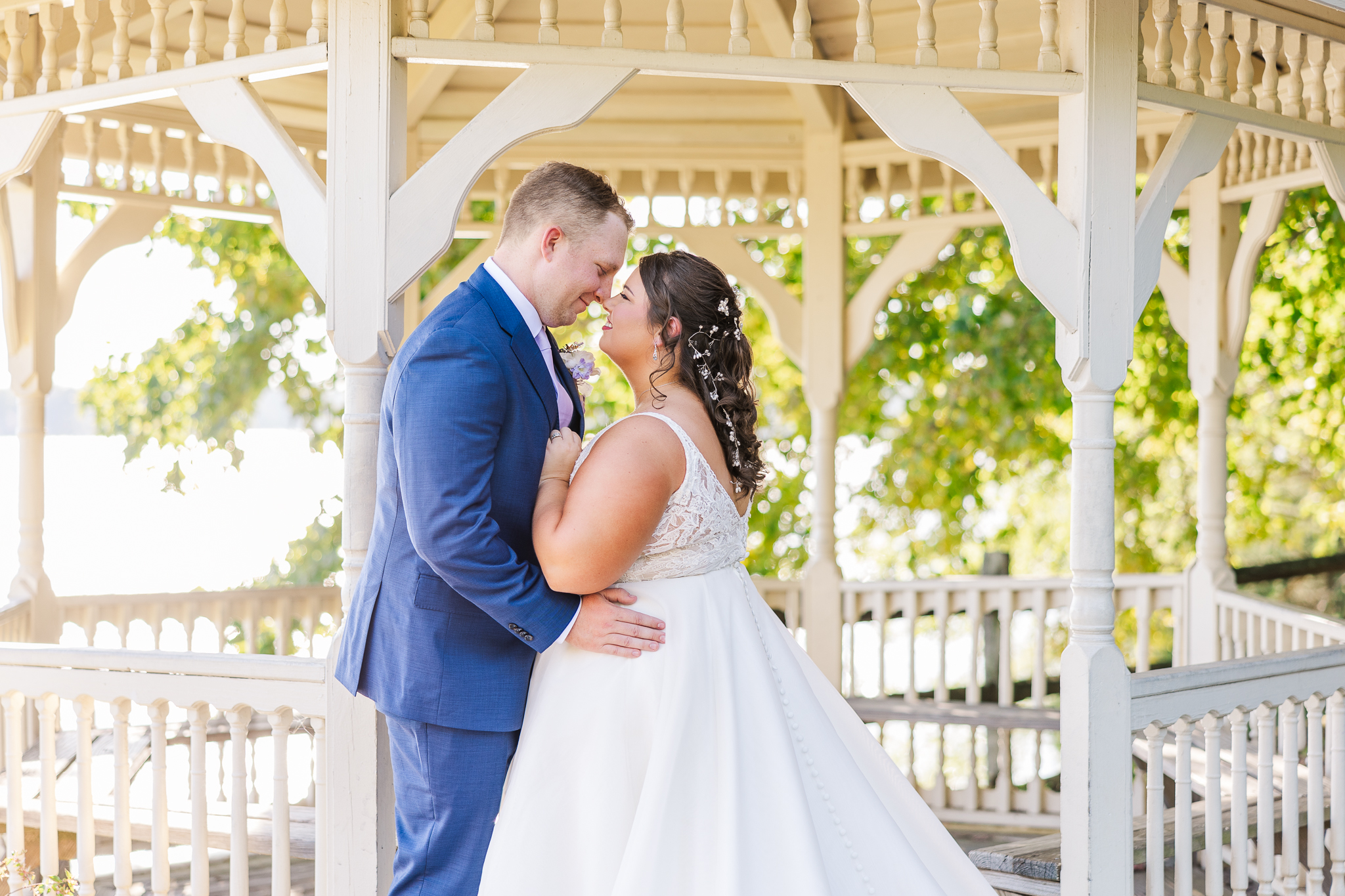 A bride and groom stand under a gazebo nuzzling noses